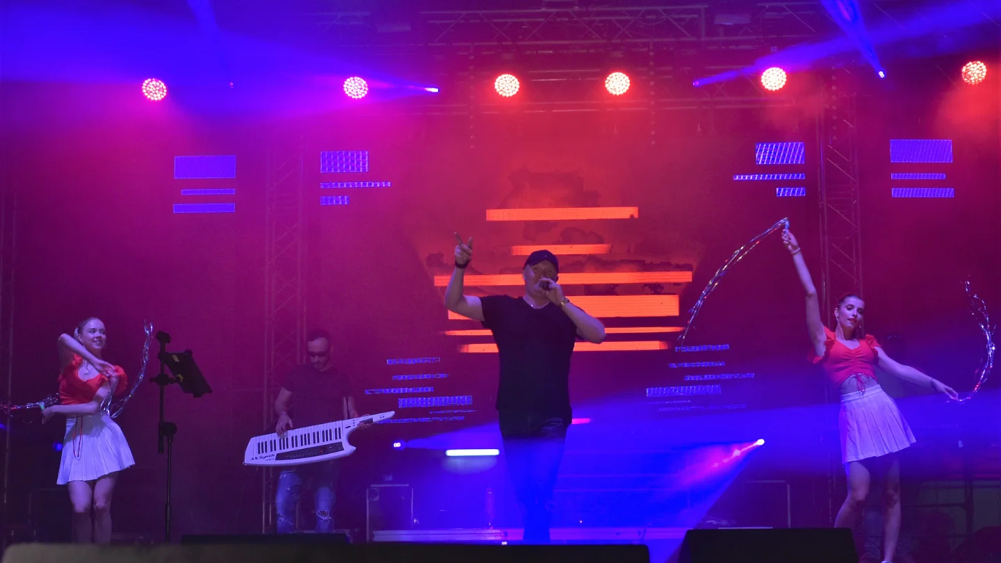 Uwodzicielski wokalista Stylovi, otoczony blaskiem sceniczych świateł, w trakcie gorącego przyjęcia publiczności na koncercie disco, emanujący energią i entuzjazmem.