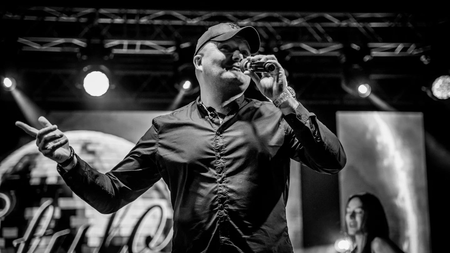 Charakteryzujący się ekspresją wokalista zespołu Stylovi, oświetlony scenicznymi światłami, przyciągający wzrok i uwagę na tle niezwykłej atmosfery koncertu discopolo.